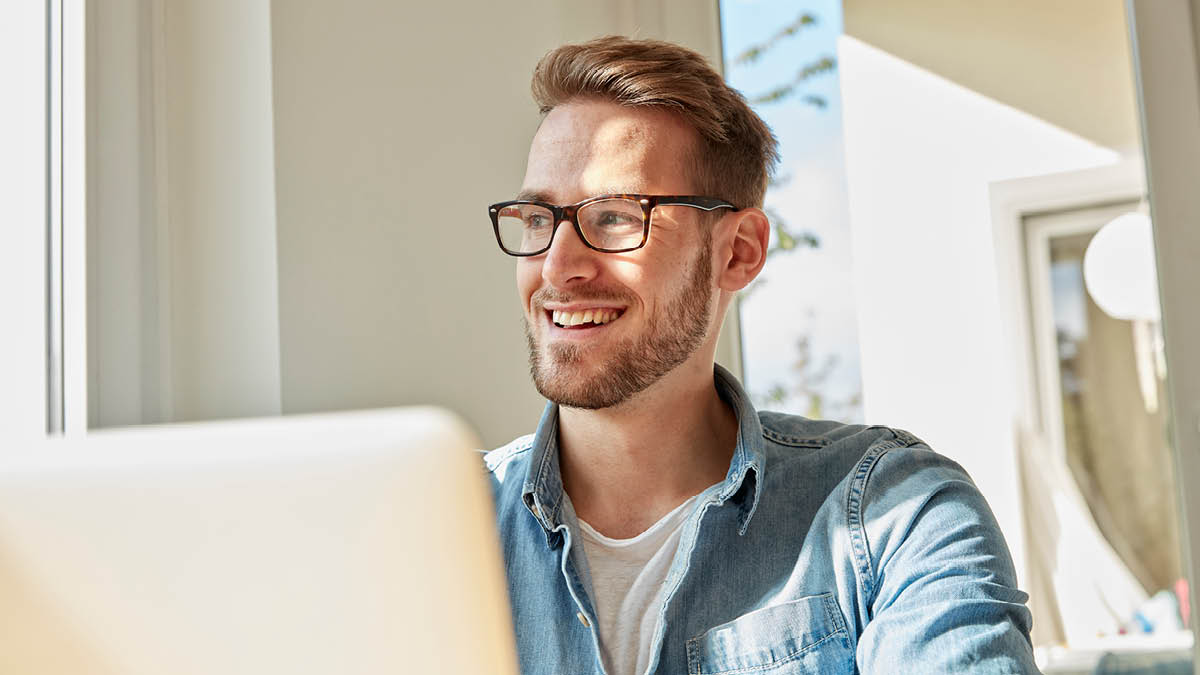 Young man sitting in front of a laptop, smiling