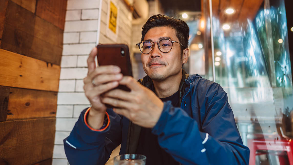 Asian man, sitting at a café table, looking at his smartphone