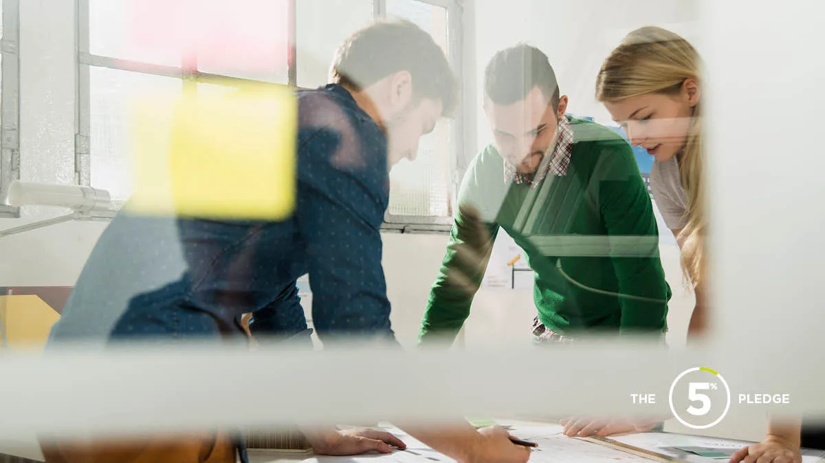 Three colleagues in a glass office looking down at plans on the desk