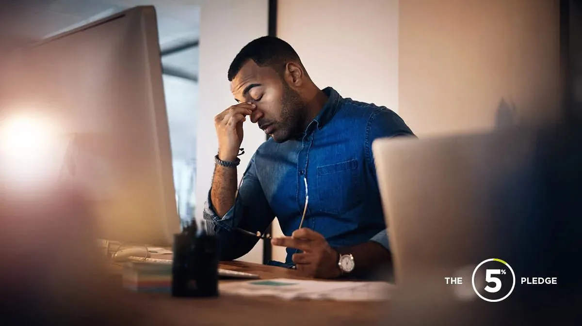 Man sitting at desk in front of two screens looking tired and stressed