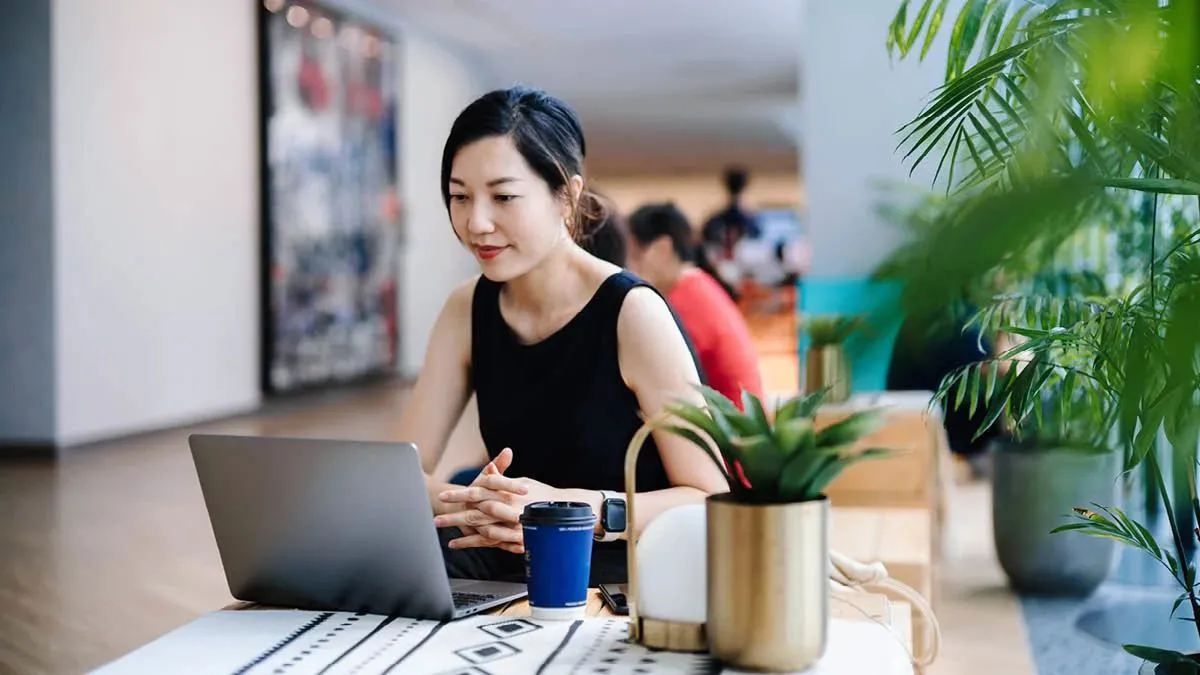 Young woman working in an open plan office at a laptop