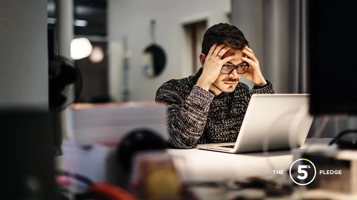 Young man sitting at a desk at night, looking at his laptop with his head in his hands