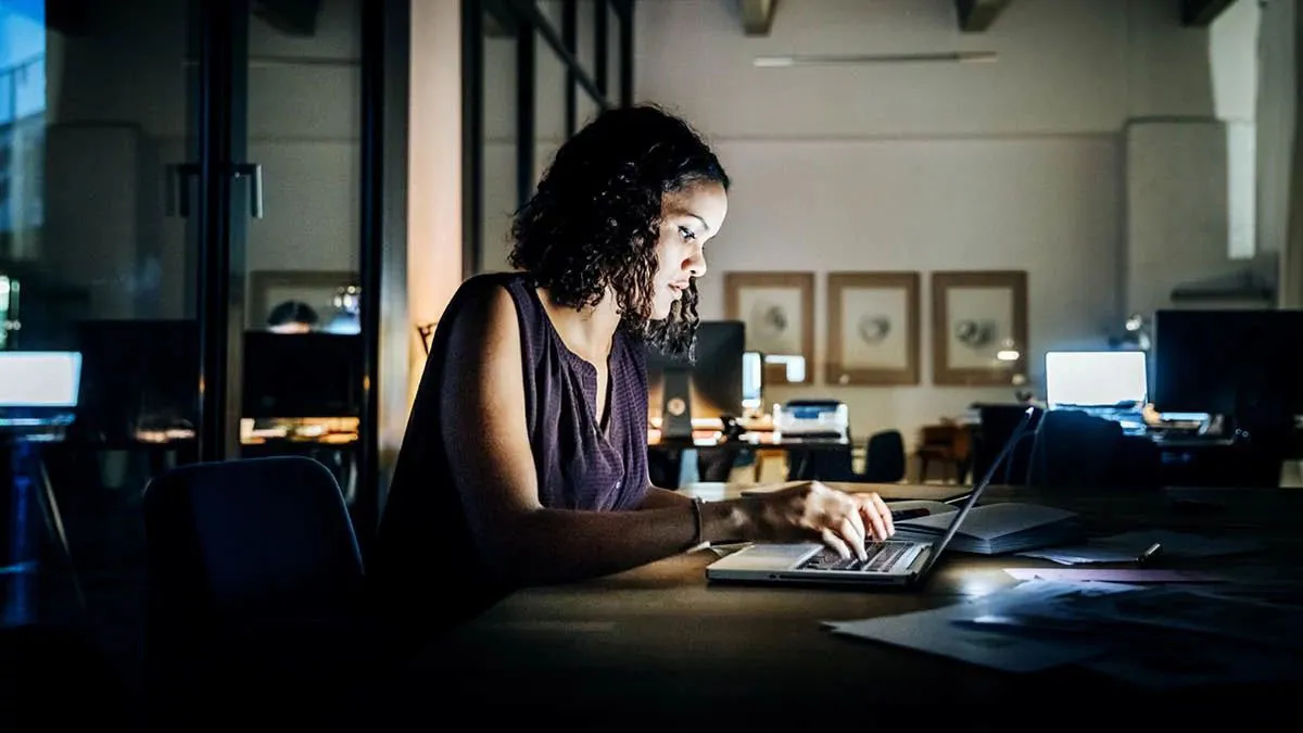 Woman sitting at her desk at night, her face is lit by the glow of her laptop