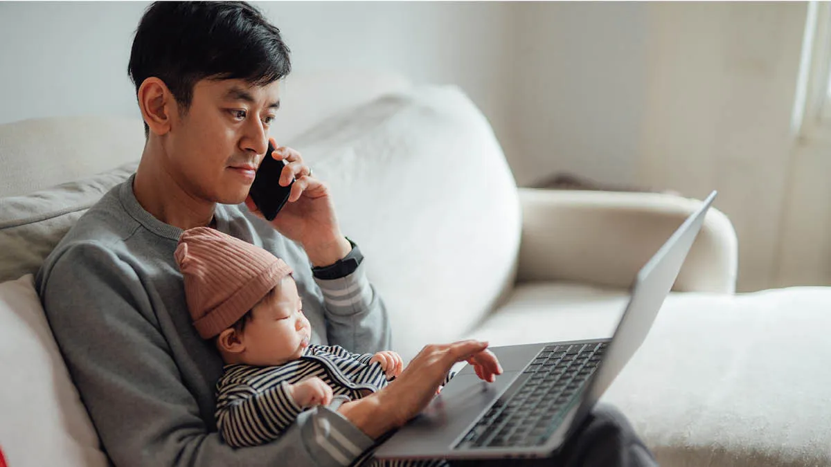 Man sitting on a sofa with a baby on his lap. He’s searching the internet and using his mobile phone