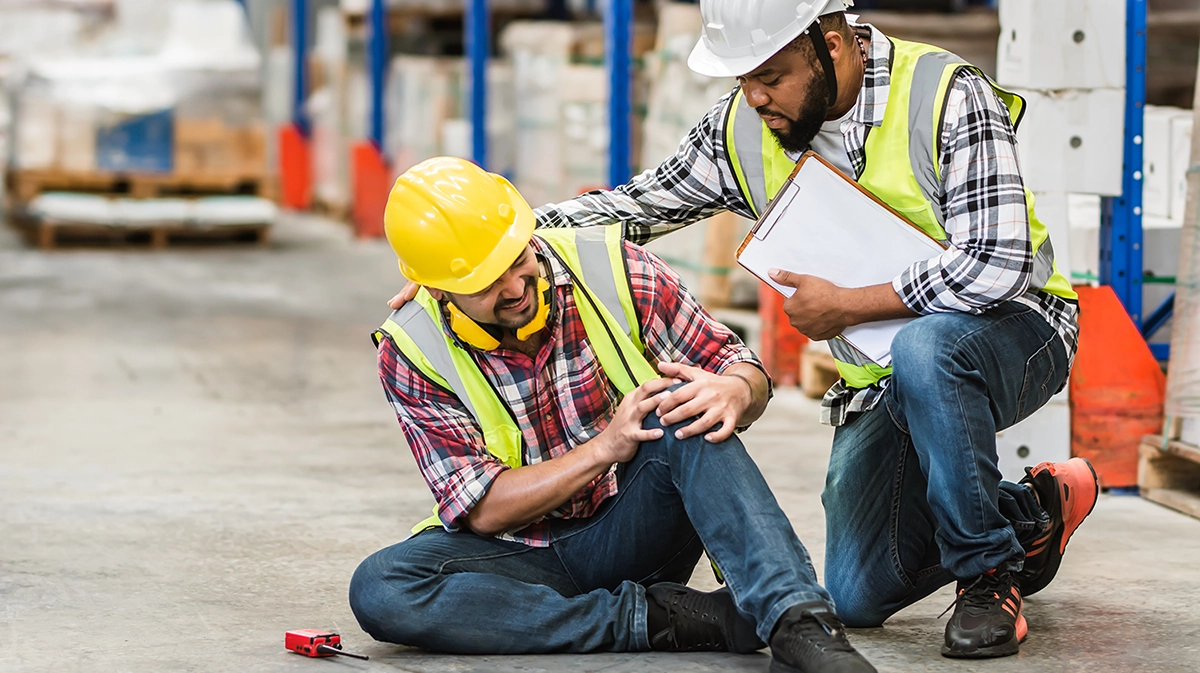 Injured employee in warehouse being helped by colleague