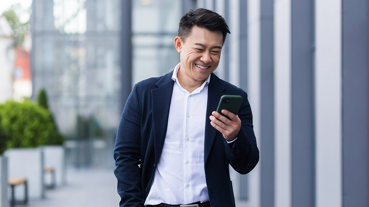 Businessman, outside offices, smiling as he reads from his mobile phone screen