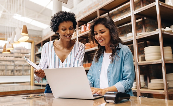 At a shop checkout, two business owners view a laptop screen