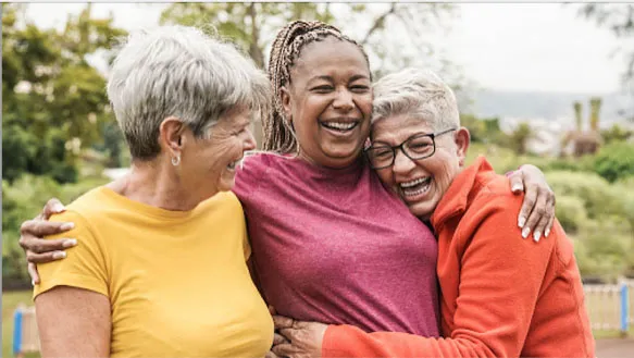 three retiree women over 50 laughing and hugging each other
