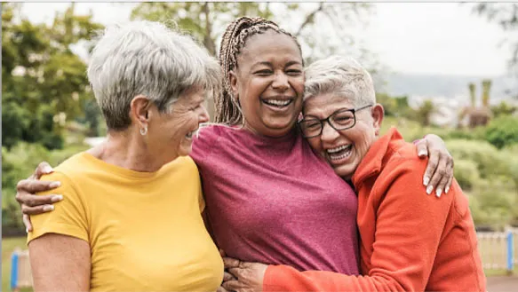 tres jubiladas de más de 50 años riendo y abrazándose