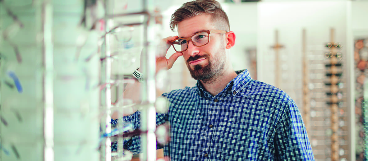 man trying on glasses and looking into a mirror