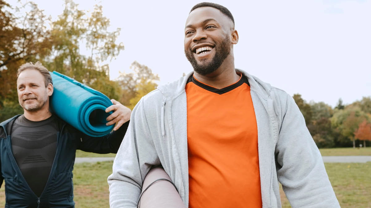 Two men, walking, holding rolled up yoga mats