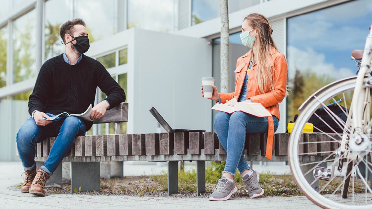 Young couple meeting outside for work wearing facemasks and keeping distance