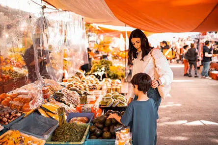 A mother and son choosing fresh vegetables at an open air market