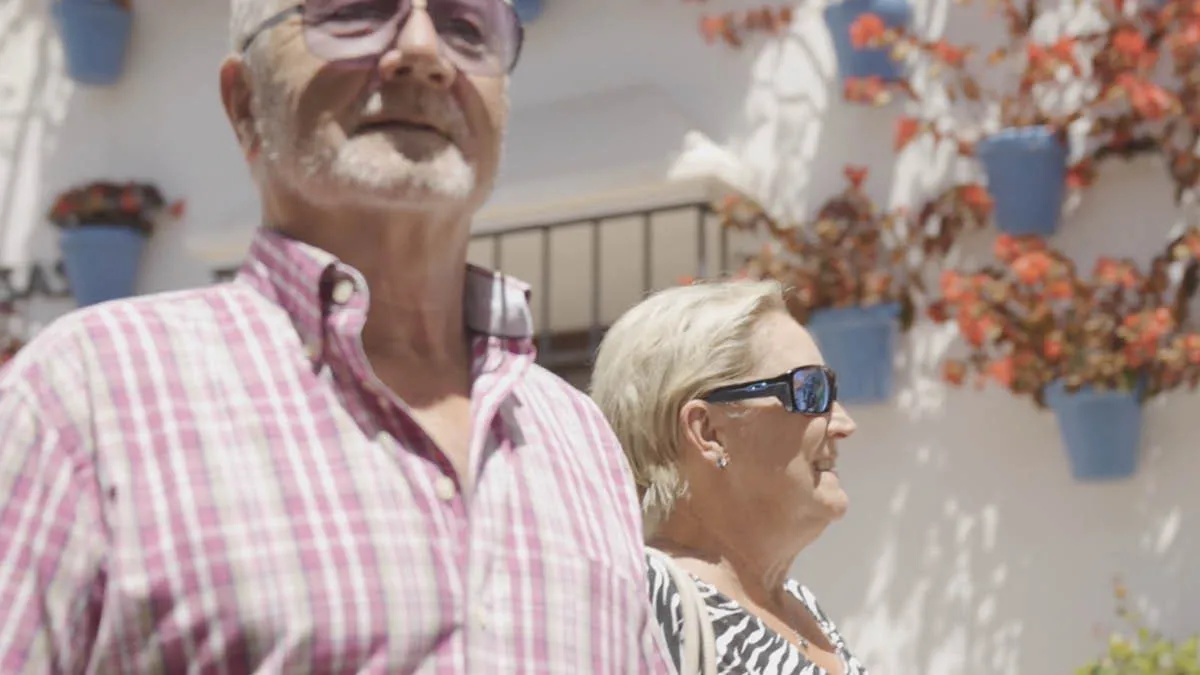British expat couple Dave and Barb walking in a Spanish town with the backdrop of a white-washed building
