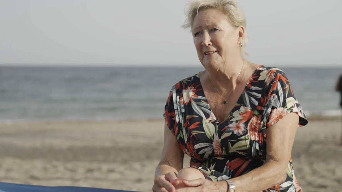 Portrait of British expat Barb sitting on the beach in Spain with the sea behind her