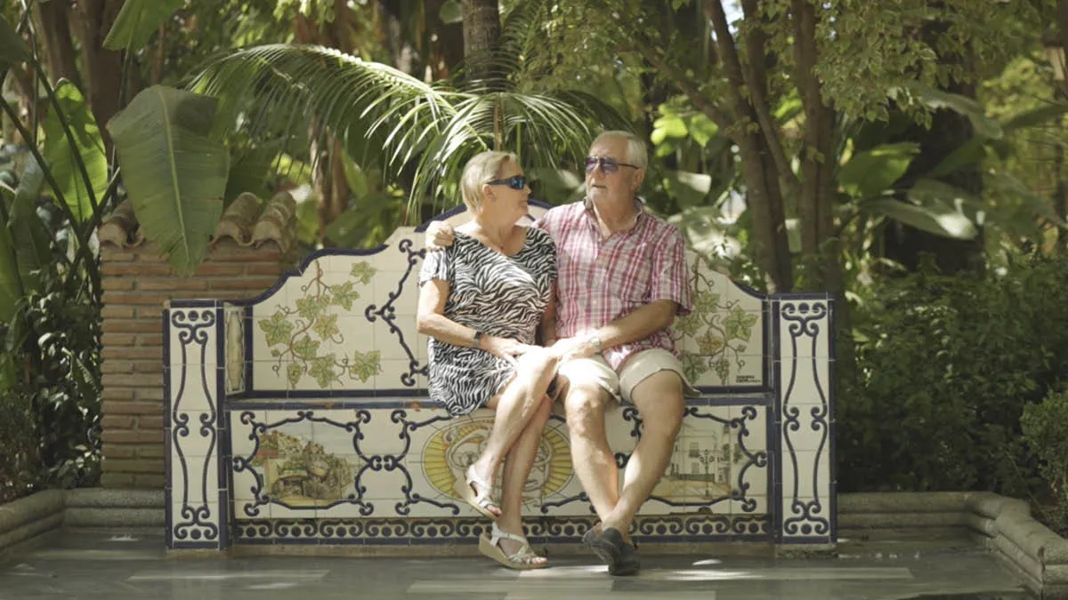 British expat couple Dave and Barb sitting closely together on an ornate bench in shade in Spain