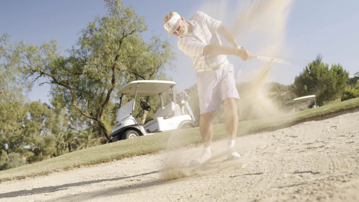 Action shot of British expat Dave hitting a golf ball in a sandy bunker on a sunny Spanish golf course