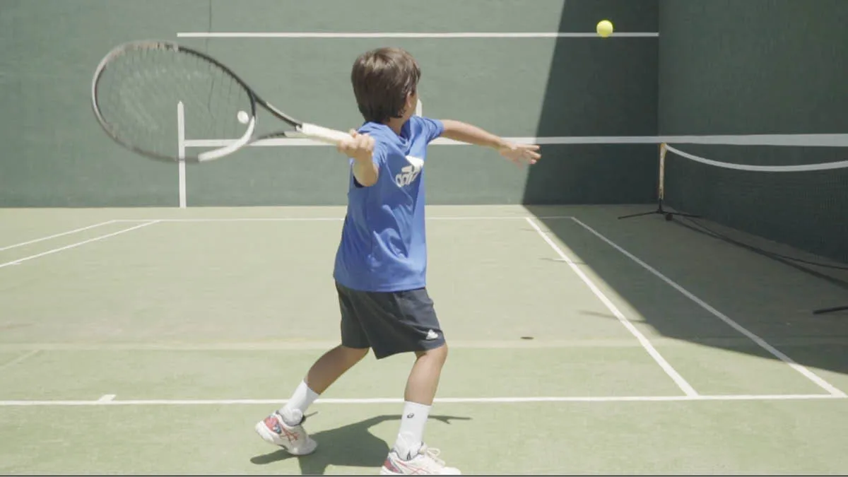 A young boy playing tennis on a court in Spain