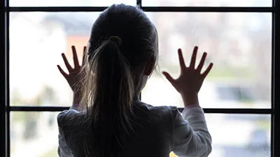 little girl in pony tail with both her hands flat on a glass window