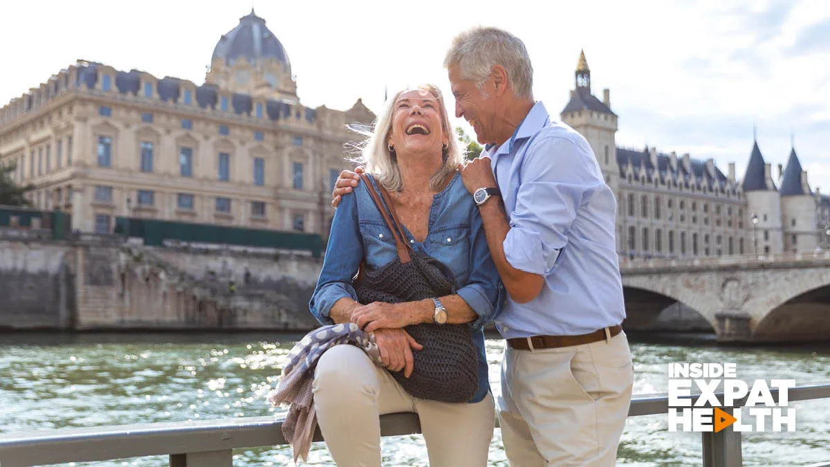An older man and woman embracing and laughing by the river in France