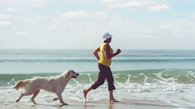 woman in yellow t shirt running along the beach with white dog