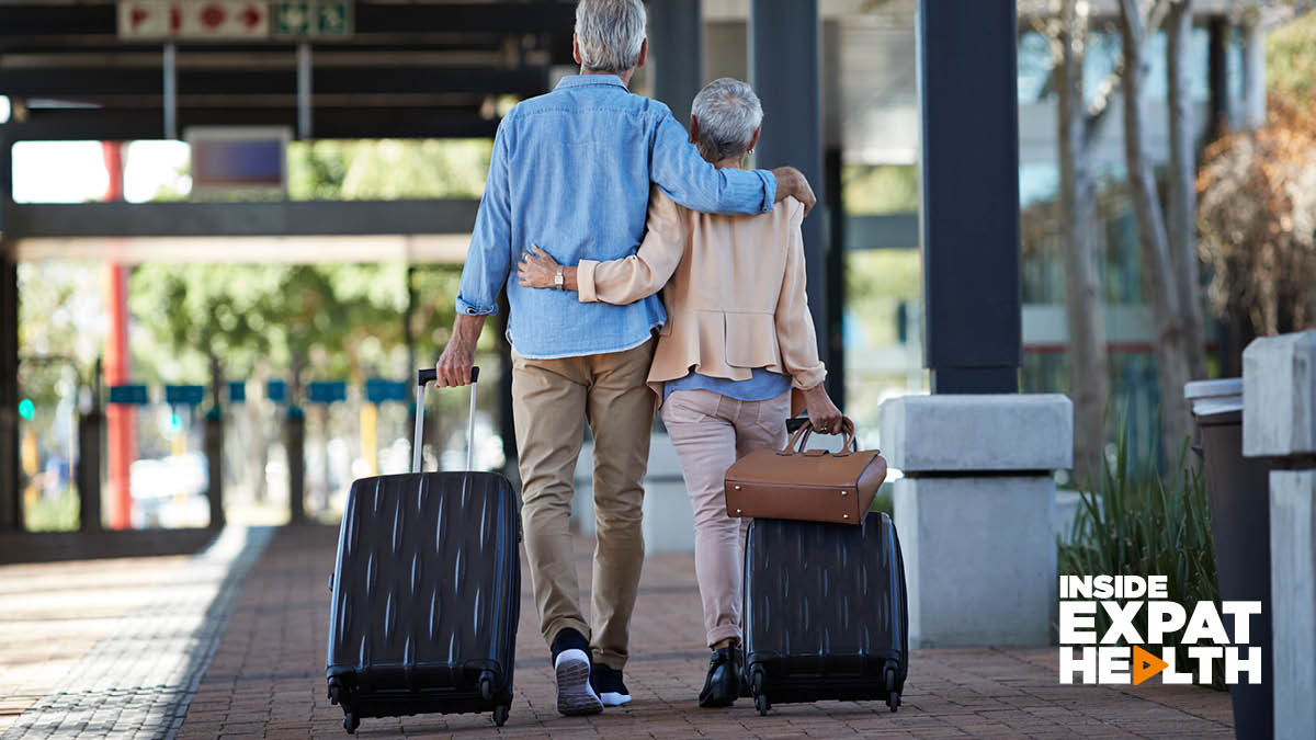 A couple walking along the street pulling suitcases, they have their arms around each other.