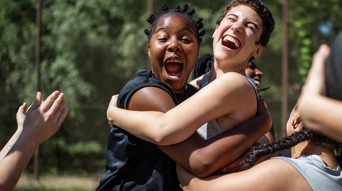 Three women jumping up, embracing each other. They are playing basketball and are celebrating