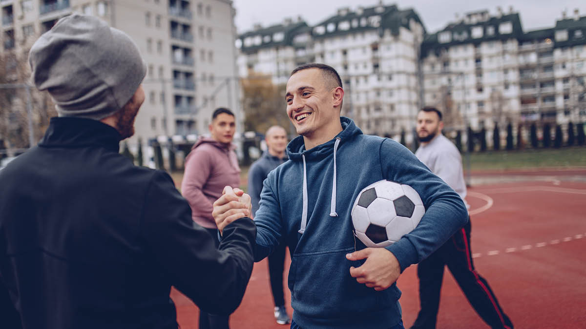 Young men playing football. One man is carrying a football under his arm while shaking another man’s hand