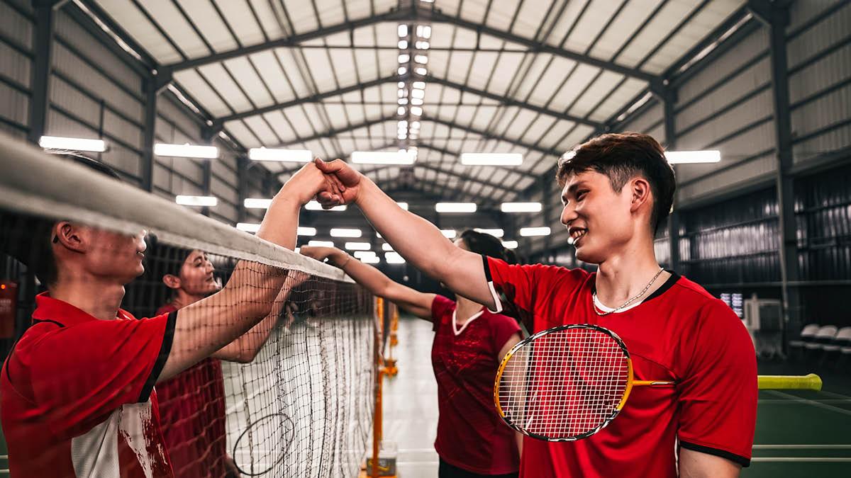 Young Asian people playing mixed doubles badminton. They are shaking their opponents’ hands over the net