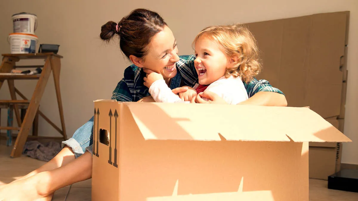 Mother and young daughter playing on the floor, the girl in in a cardboard box