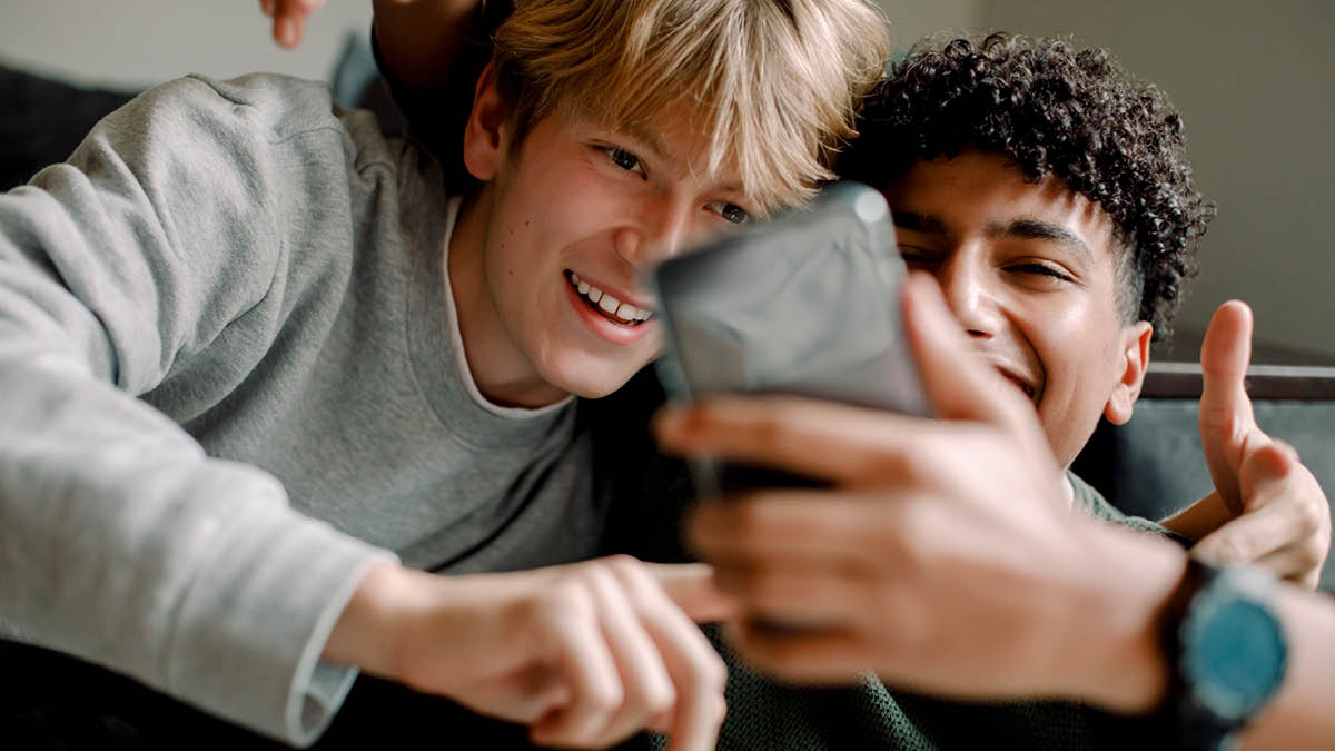 Two teenage boys laughing while looking at a mobile phone
