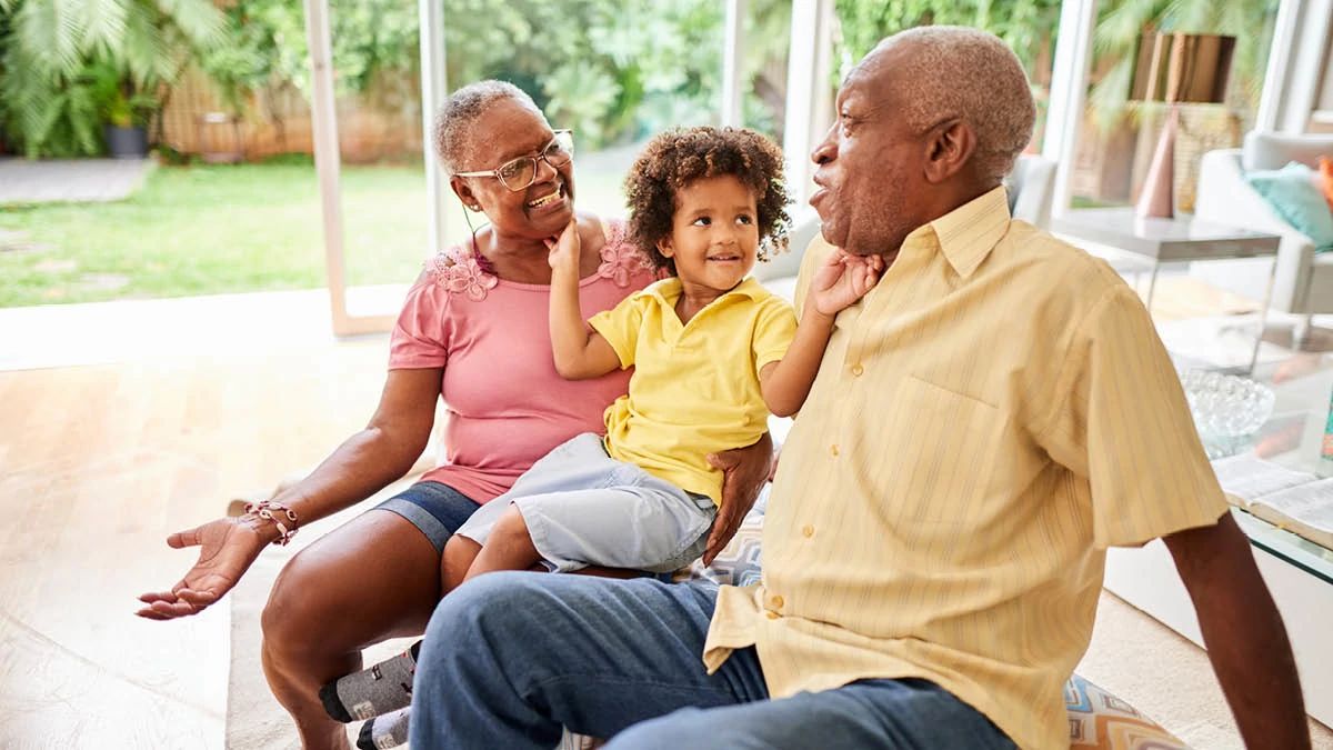 grandparents with toddler on their lap at home touching their faces and laughing together