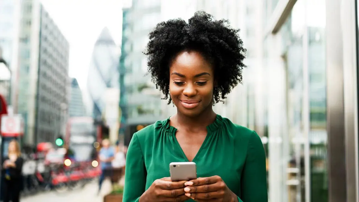woman in green top smiling looking at phone in London street