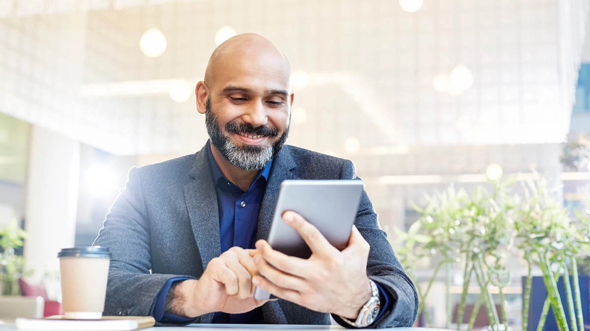 Smiling man sitting down having coffee and looking at a tablet