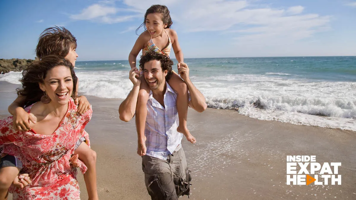 A happy family walking along a sandy beach. The son is having a piggy back from his mother, the daughter is on her father’s shoulders