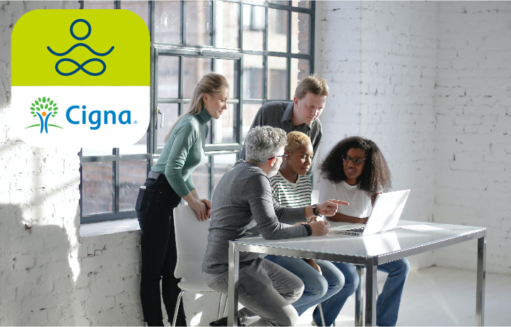 A group of people huddled around a laptop working together in a calm, naturally lit workroom.