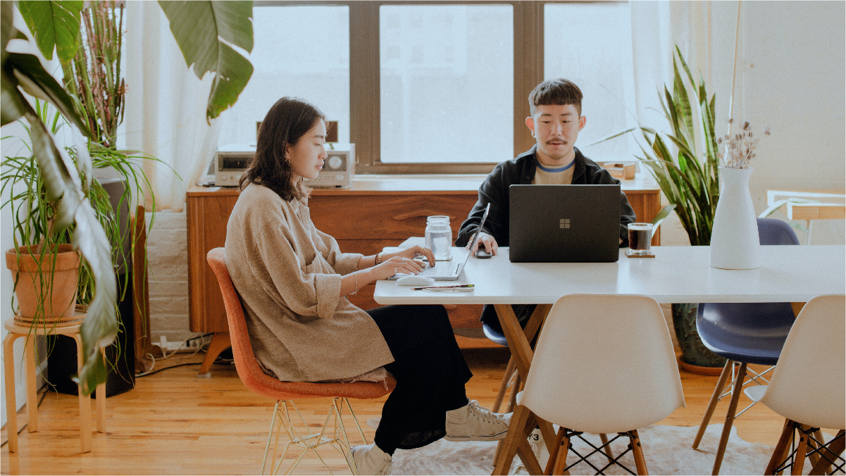 A young professional couple sits at their dining room table quietly working from home together.